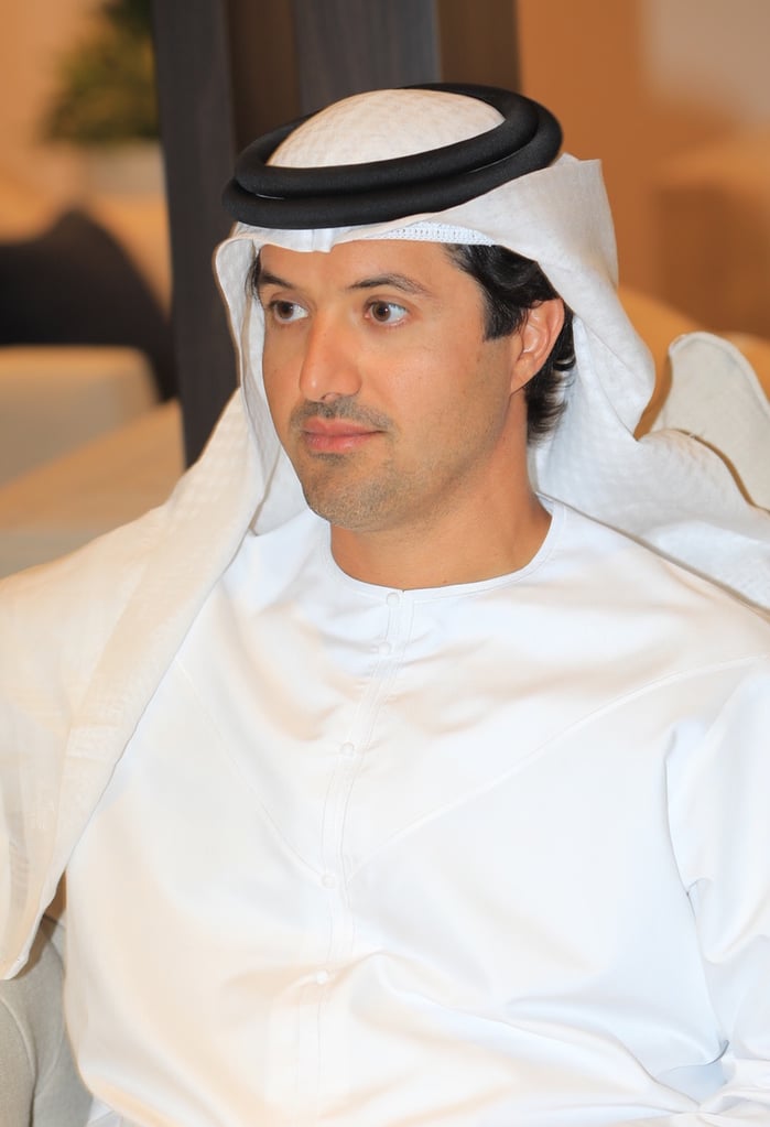 Man in traditional Middle Eastern attire seated in a light-colored room.