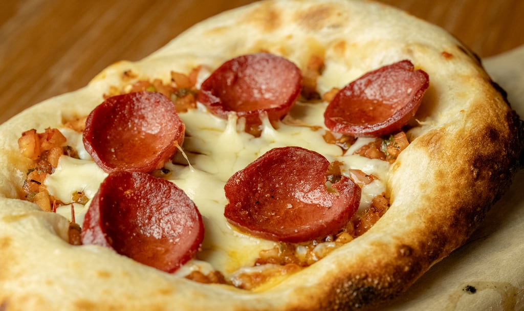 Pizza with melted cheese and pepperoni slices on parchment paper.