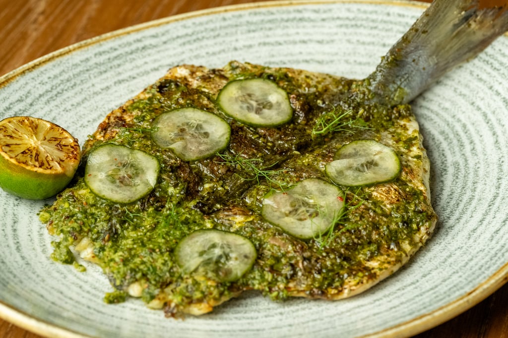 Grilled fish with green sauce and cucumber slices on a plate.