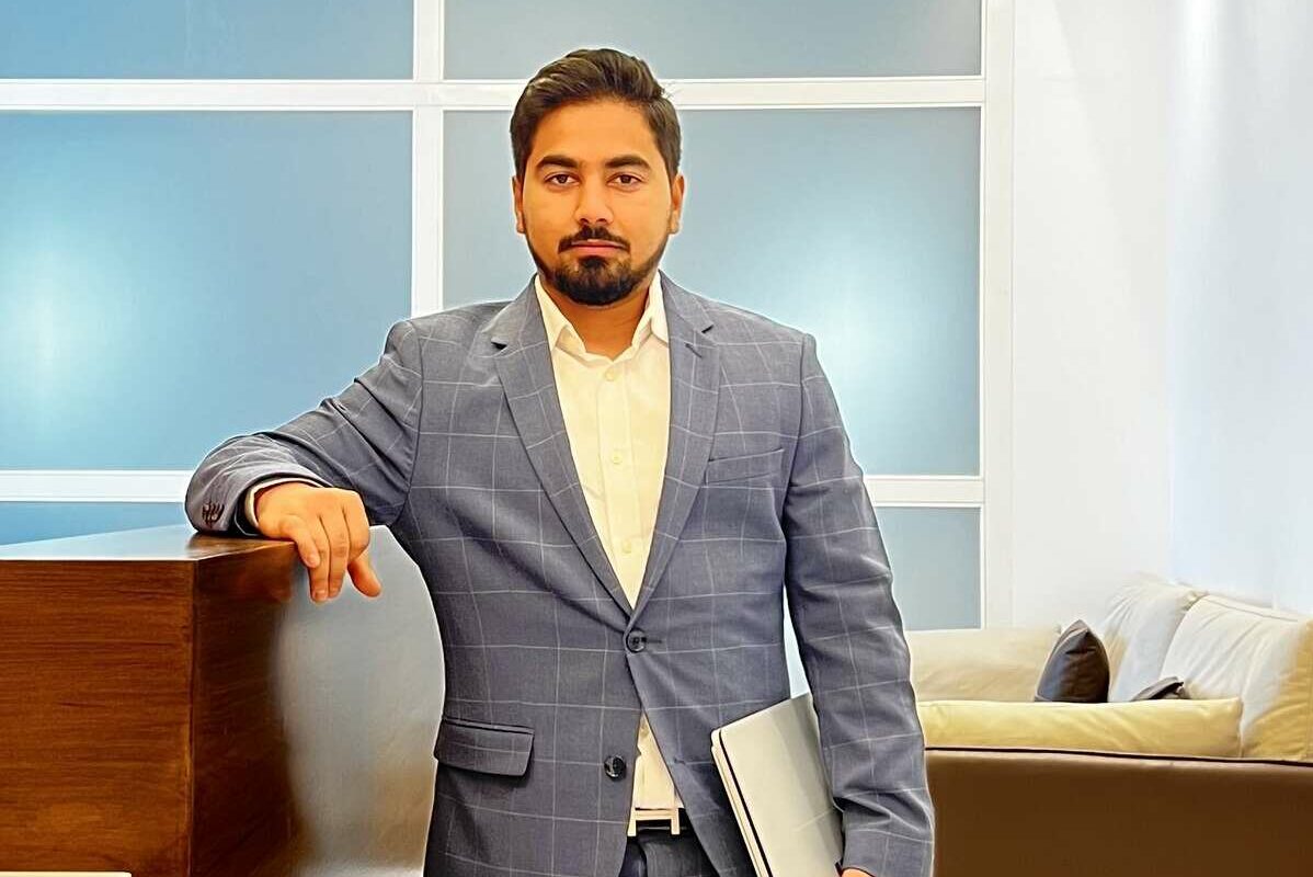 Man in gray suit holding laptop in modern office.