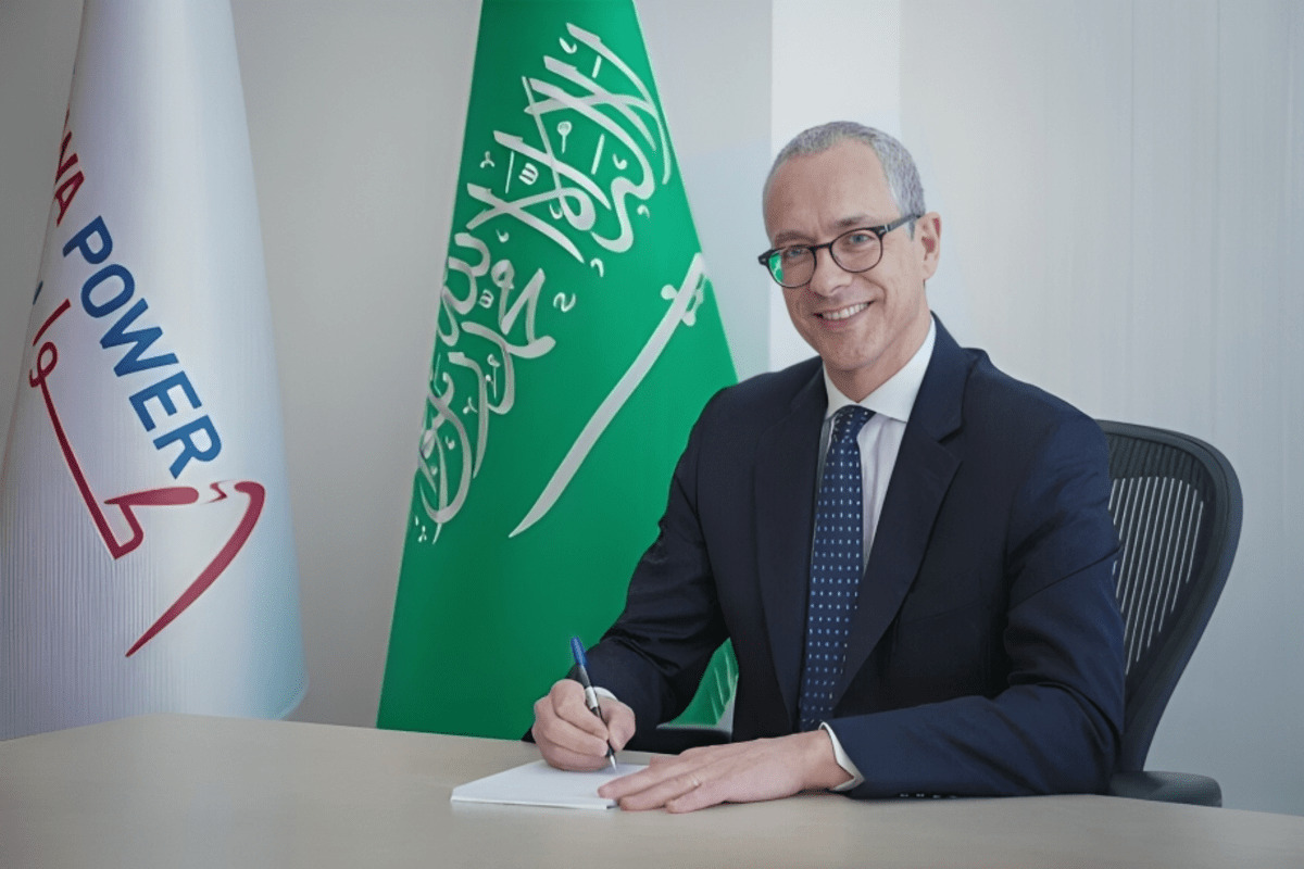 Man signing a document with Saudi Arabian and ACWA POWER flags.