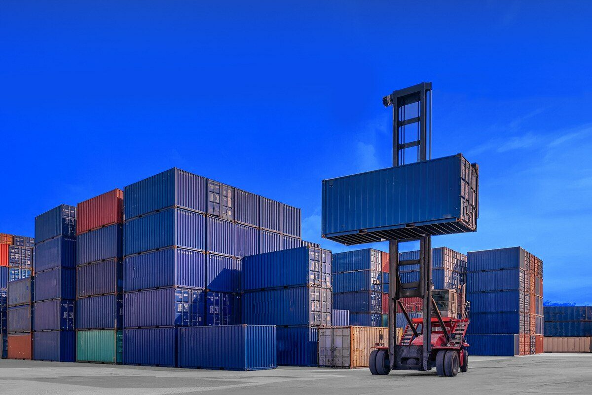 Forklift lifting a shipping container under a clear blue sky.