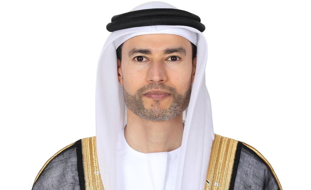 A man in a white keffiyeh and black kandura poses against a white background.