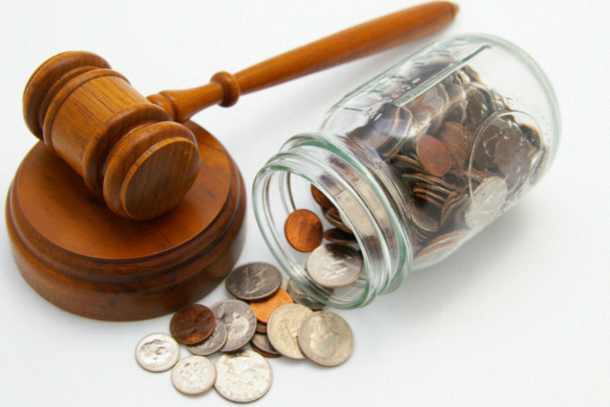 Wooden gavel near spilled coins on a white surface.