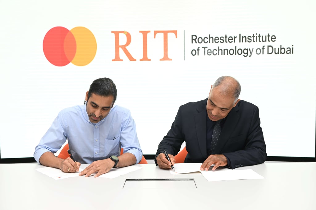 Two men signing documents with RIT and Mastercard logos behind them.