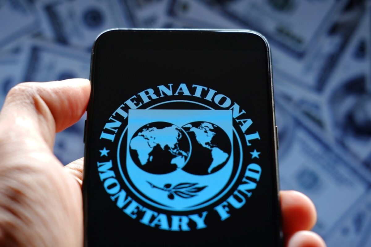 Smartphone with IMF logo held over dollar bills.
