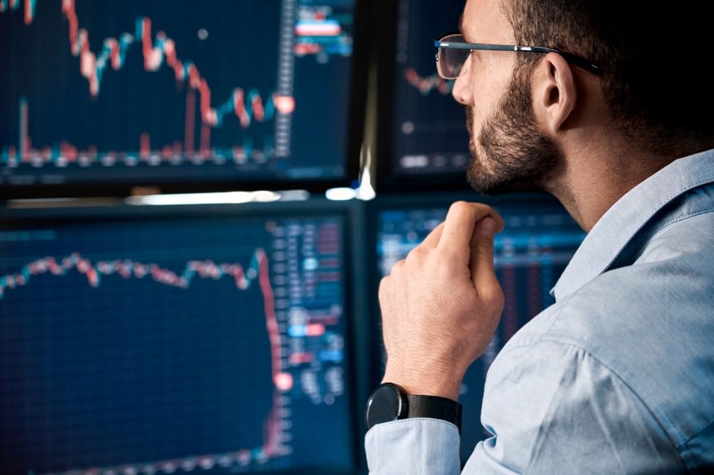 Man analyzing stock data on monitors in a dim office.