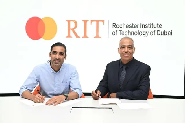 Two men signing documents with Mastercard and RIT logos.