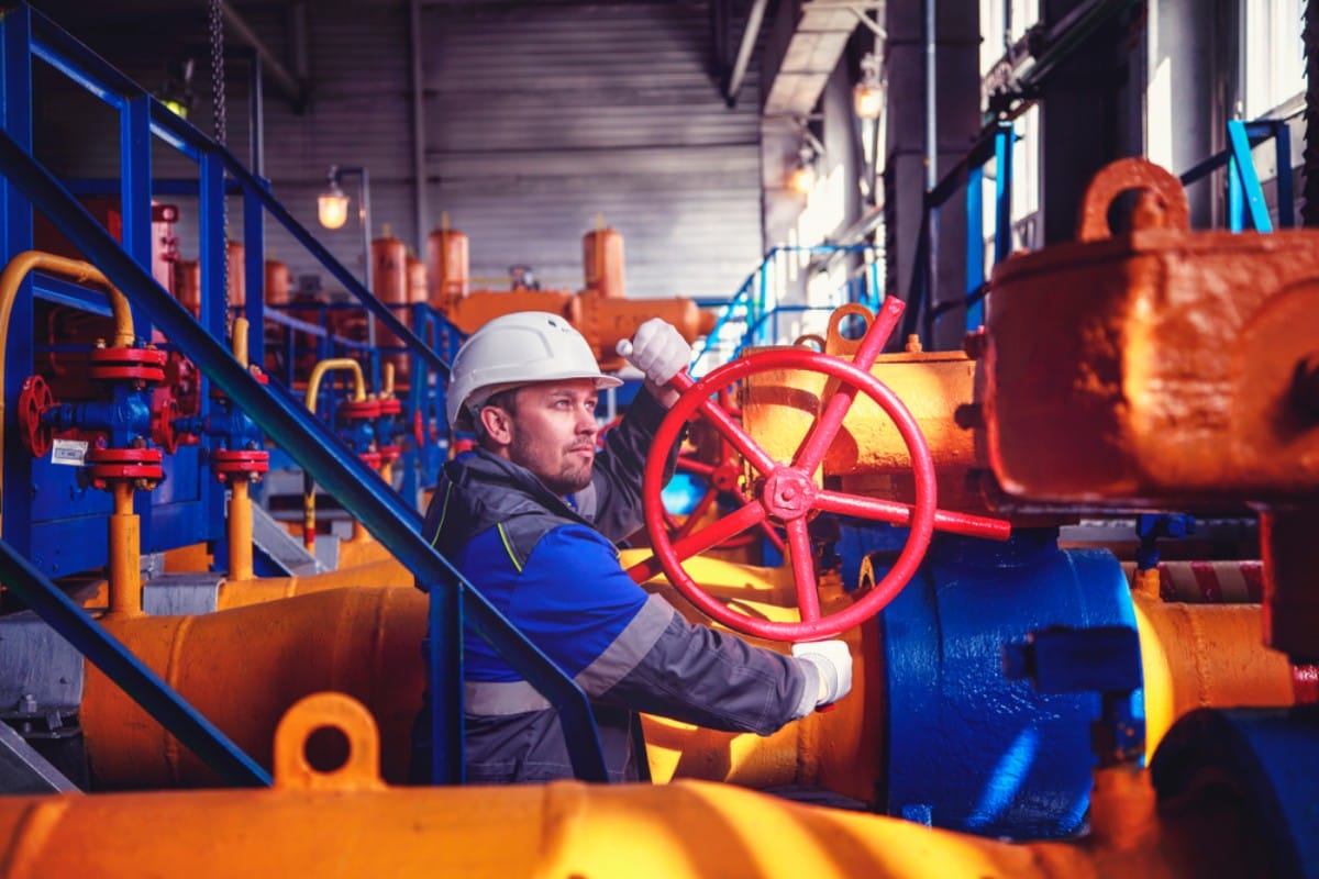 Worker adjusting a large valve in an industrial plant.