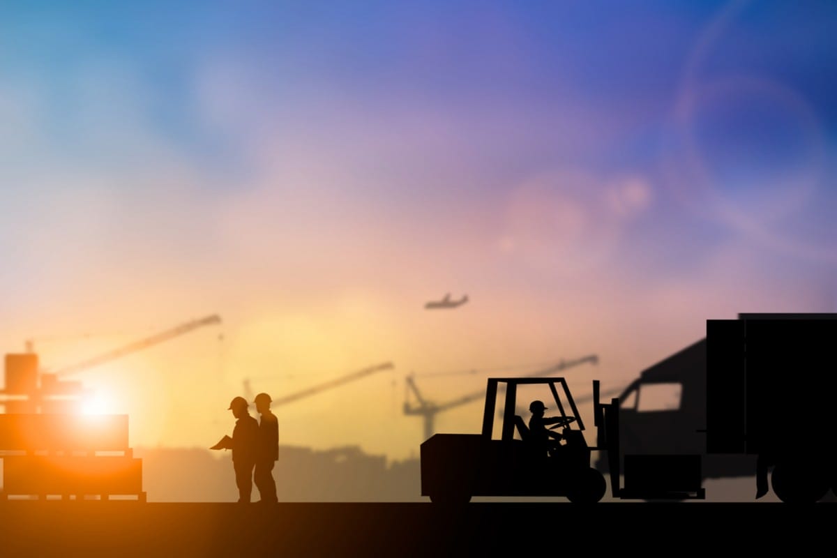 Workers overseeing boxes being moved by a forklift at sunset.