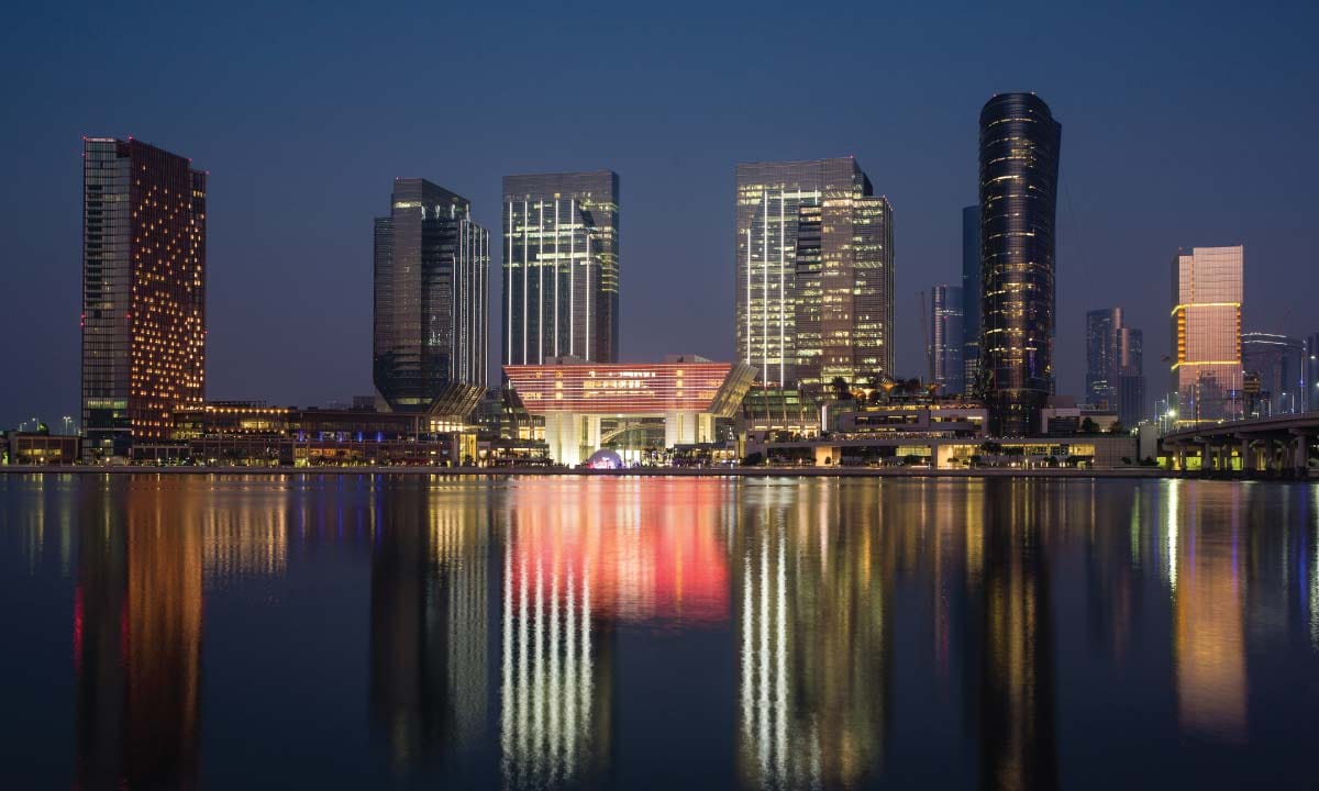 Skyscrapers illuminated at night reflecting in calm water.
