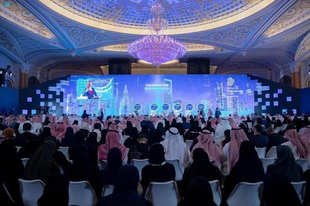 Conference audience; a speaker on a screen shows 