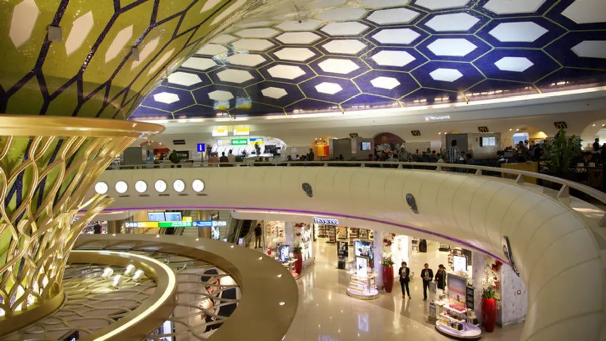 Ornate golden structure in an airport terminal with people shopping below.