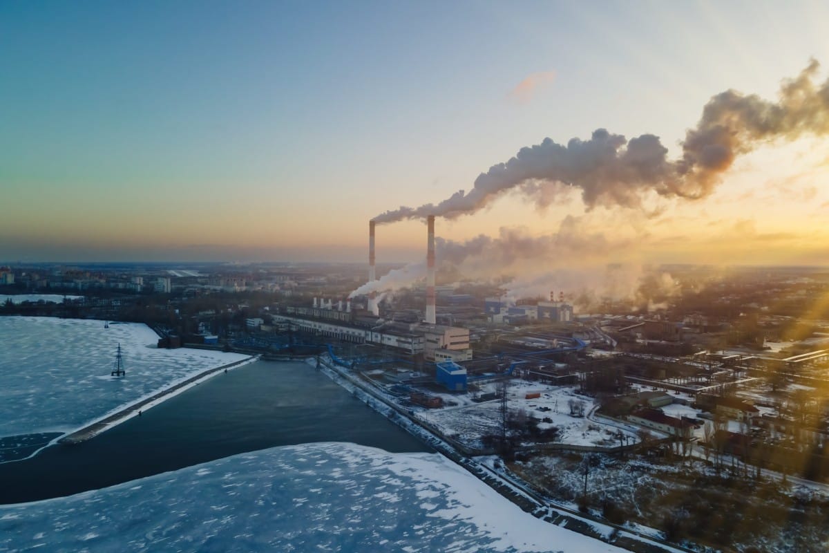 Power plant emitting smoke at sunset on a riverbank in winter.