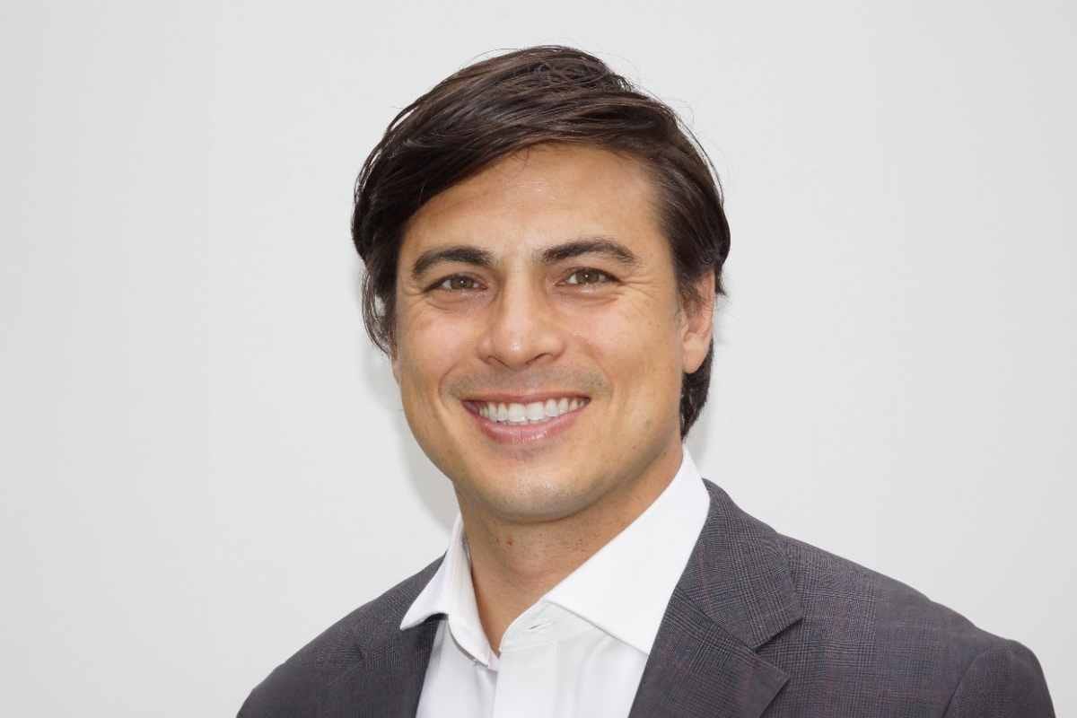Man in a gray suit and white shirt smiling against a white background.
