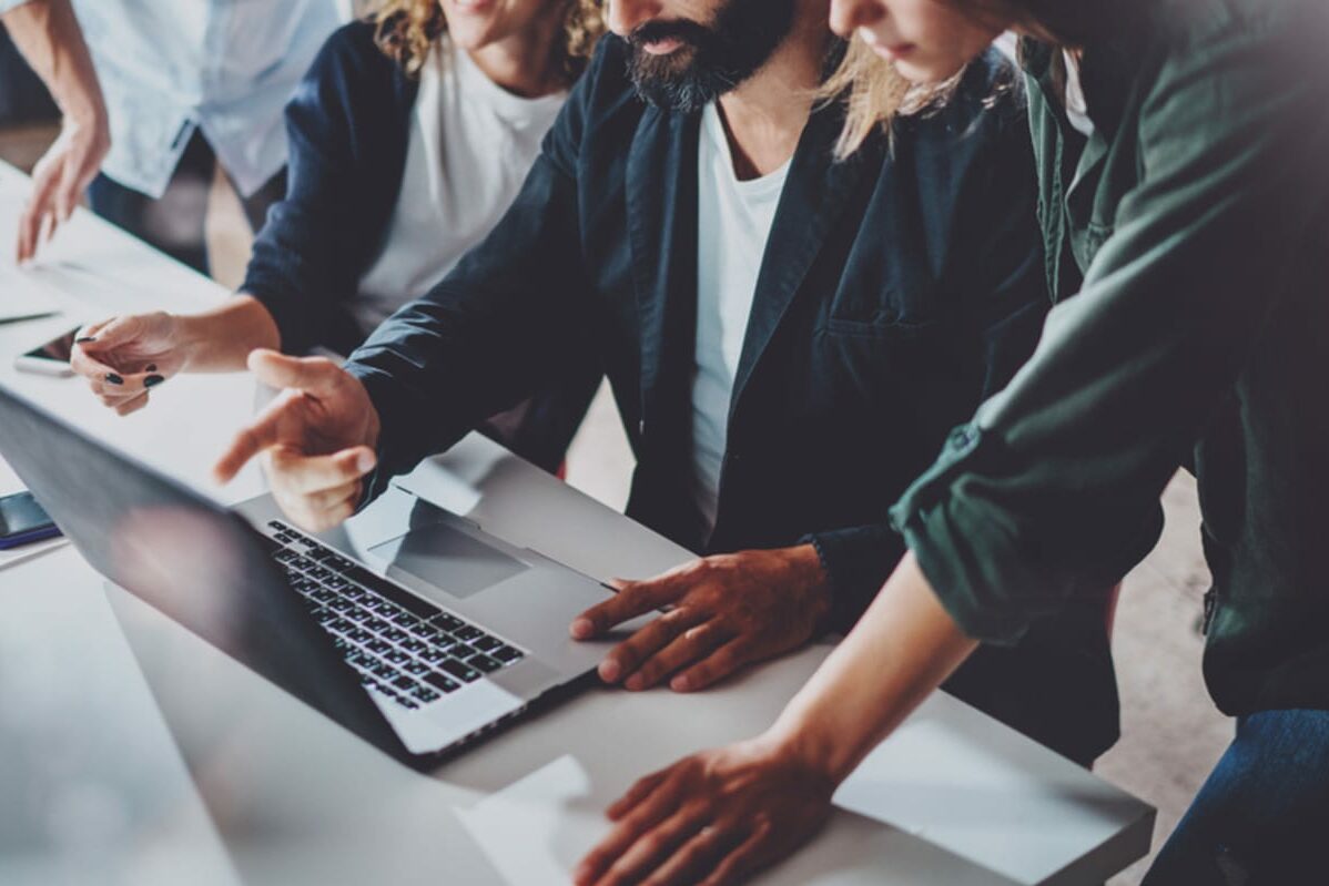 Man and two women reviewing laptop in a bright office.