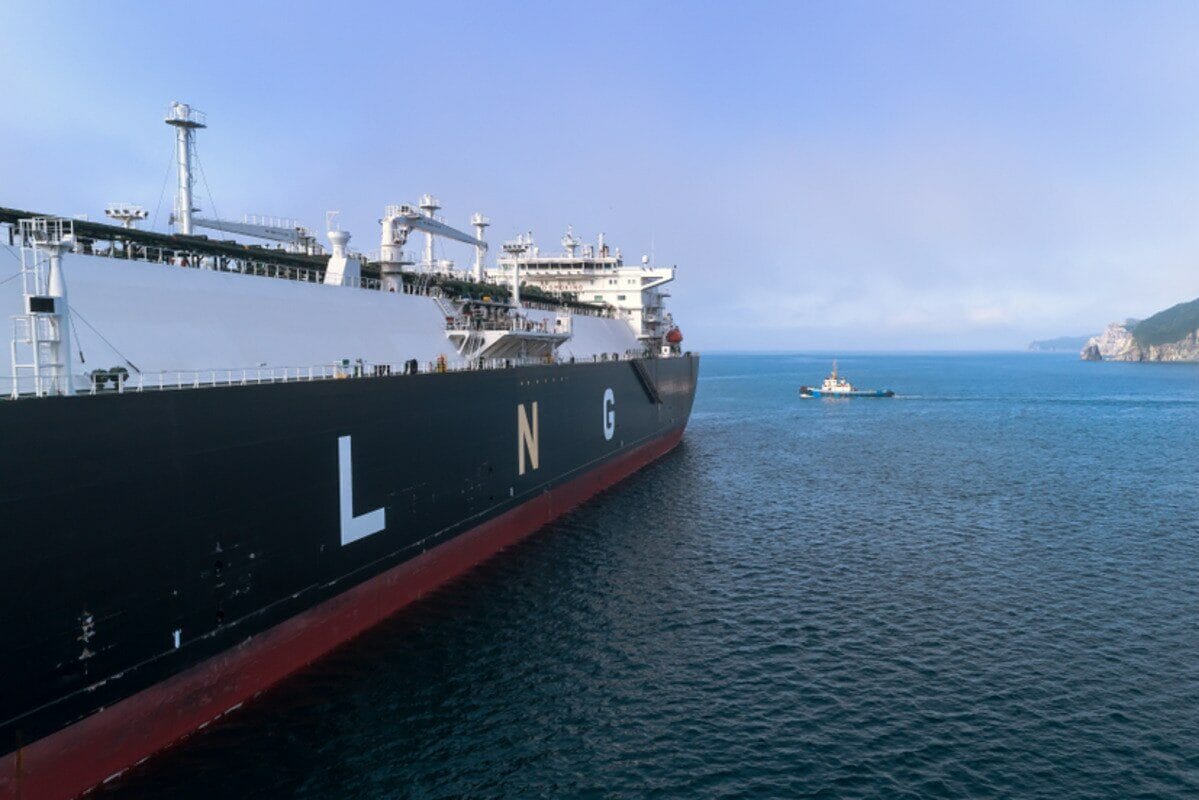 LNG carrier sailing on the open ocean with a tugboat in the distance.