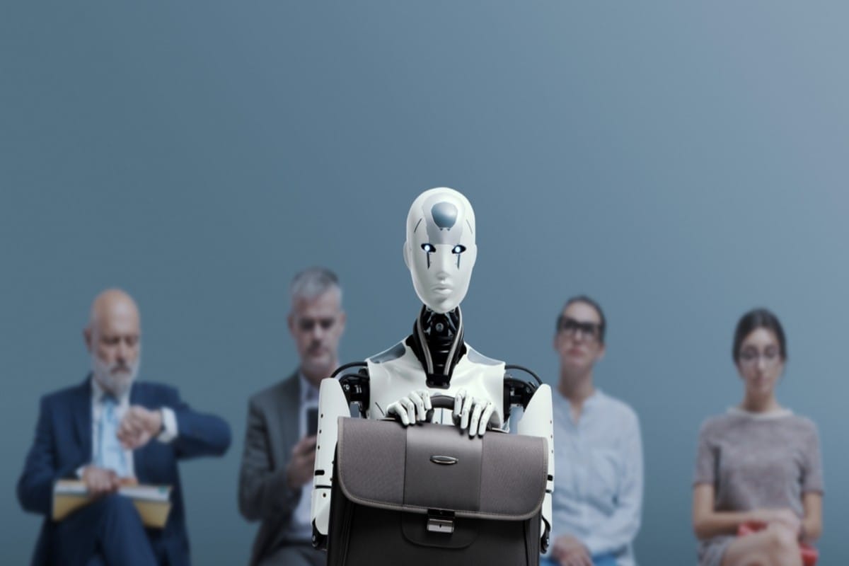 Humanoid robot holding a briefcase in front of seated interviewers.