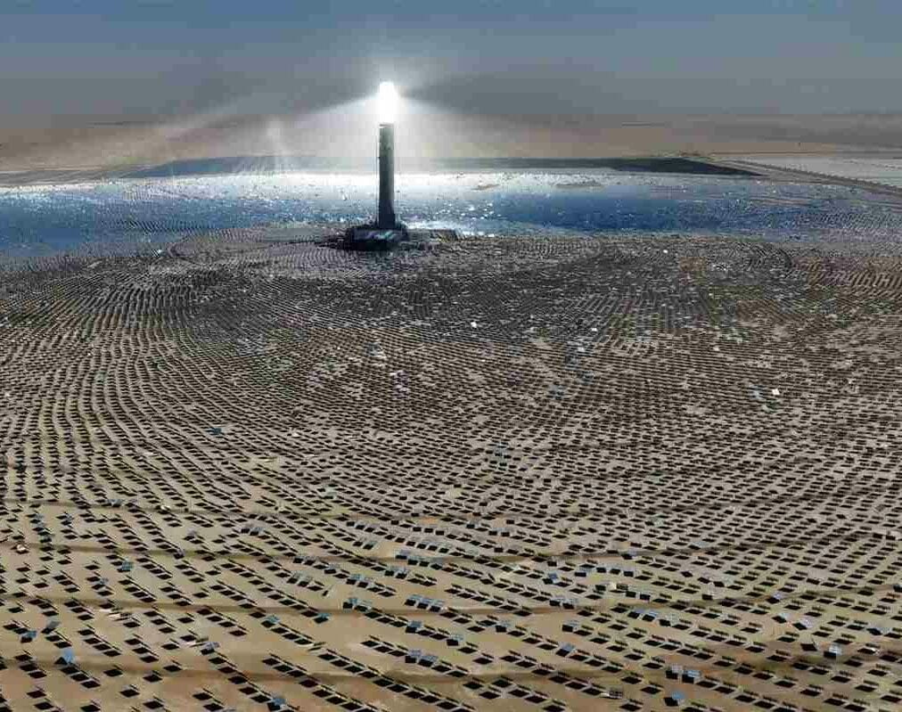 Solar tower concentrating sunlight onto a field of solar panels in a desert.