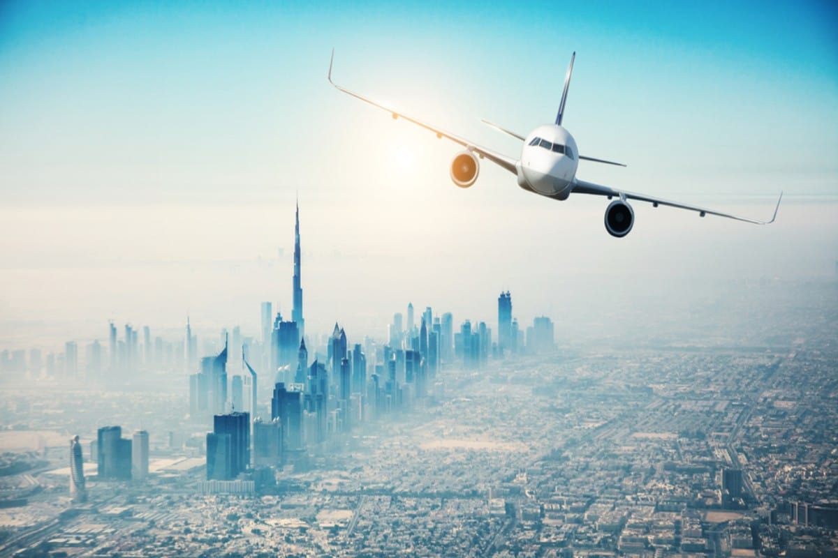 Passenger airplane flying over a hazy cityscape with Burj Khalifa visible.