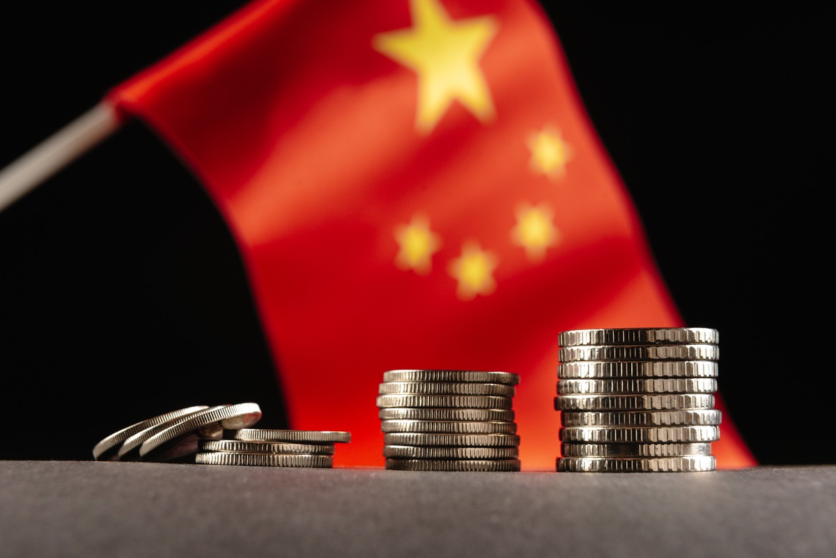 Stacks of coins with a blurred Chinese flag in the background.