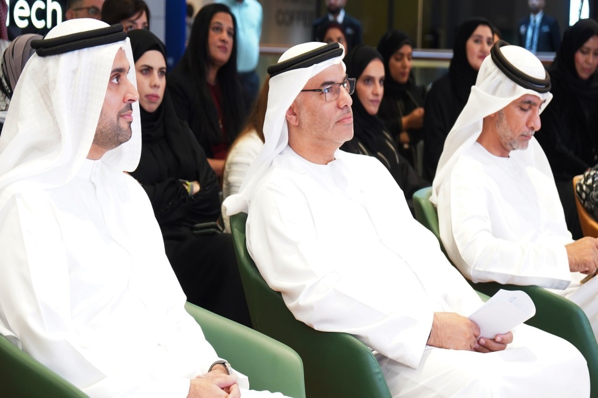Three men in white thobes seated at an indoor event.
