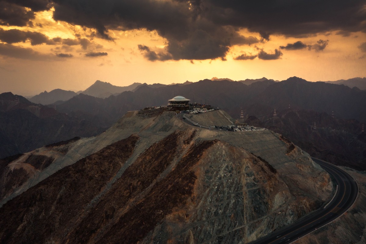 Dome-shaped structure on mountain with winding road and sunset view.