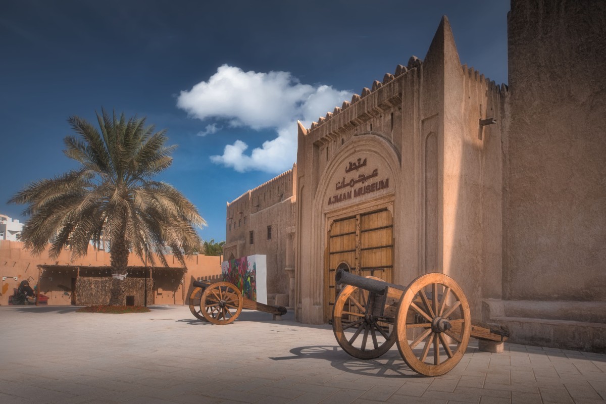 Cannons outside Ajman Museum with Arabic signage.