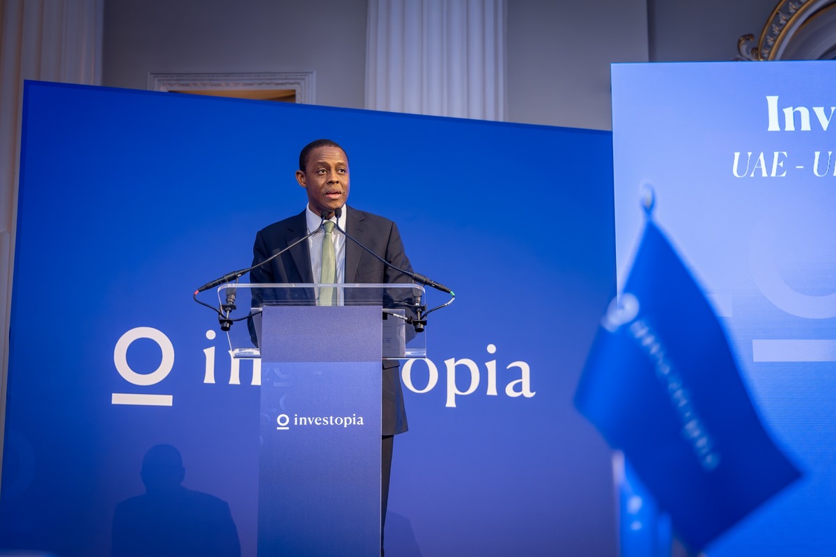 Man speaking at podium at formal event with "O investopia" logo.
