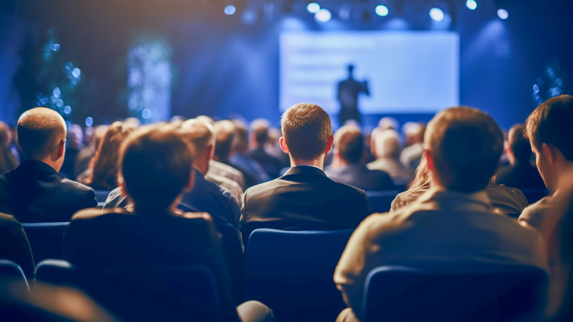 Audience listening to a presentation in a dimly lit auditorium.