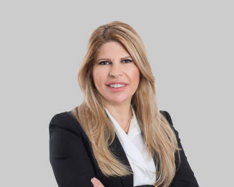 Blonde woman in a blazer smiling against a grey background.