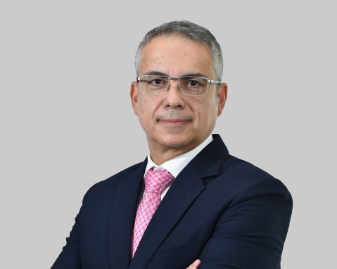 Man in a suit with glasses stands with arms crossed.
