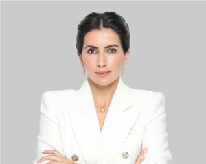 Woman in a white blazer posing with arms crossed against a gray background.