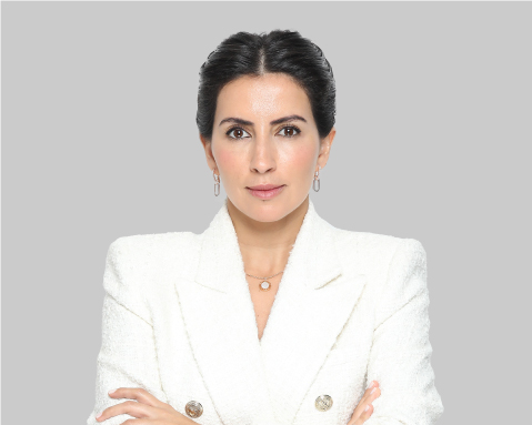 Woman in a white blazer posing with arms crossed against a gray background.