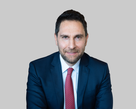 Man in blue suit and red tie sits against gray background.