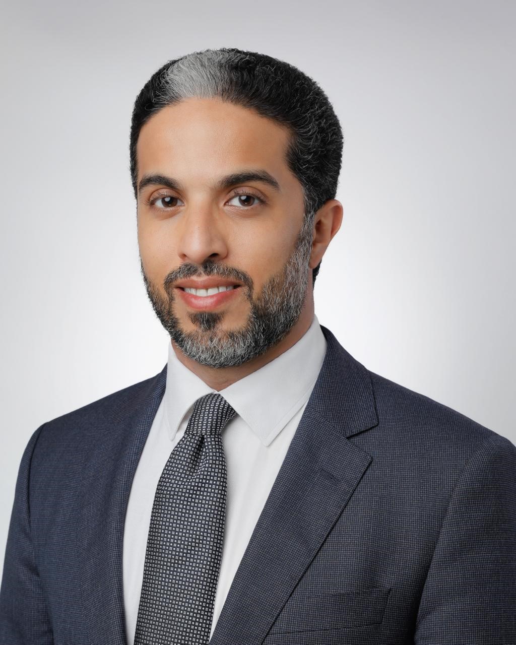 Smiling man in dark suit against a light gray background.