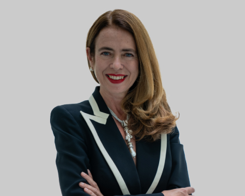 Woman in a dark jacket with arms crossed against a light gray background.