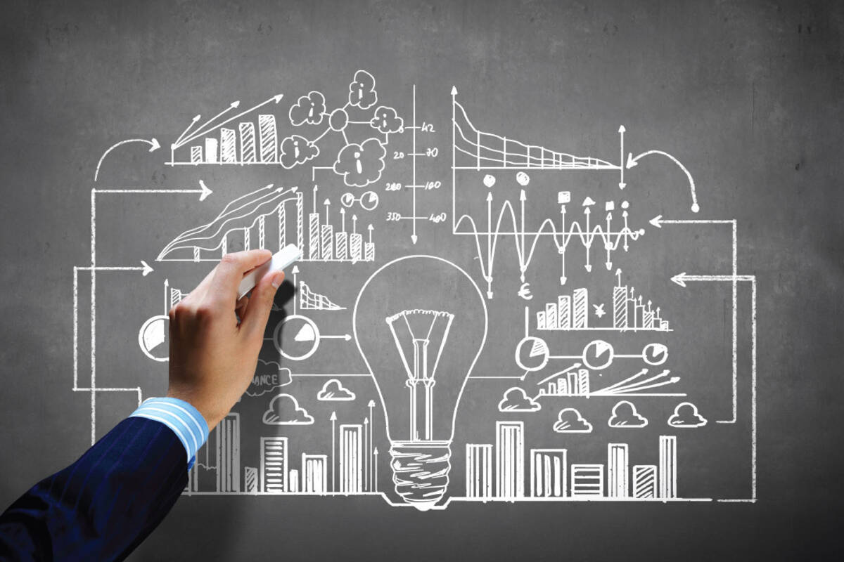 Hand draws a lightbulb and business charts on a dark gray chalkboard.