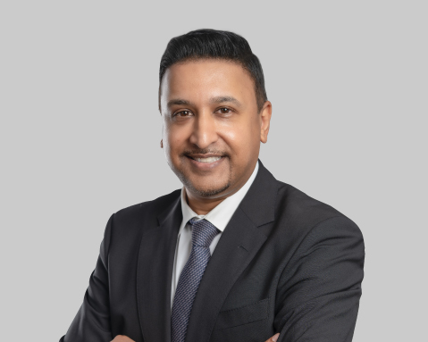 Man in a dark suit and tie, smiling with arms crossed.