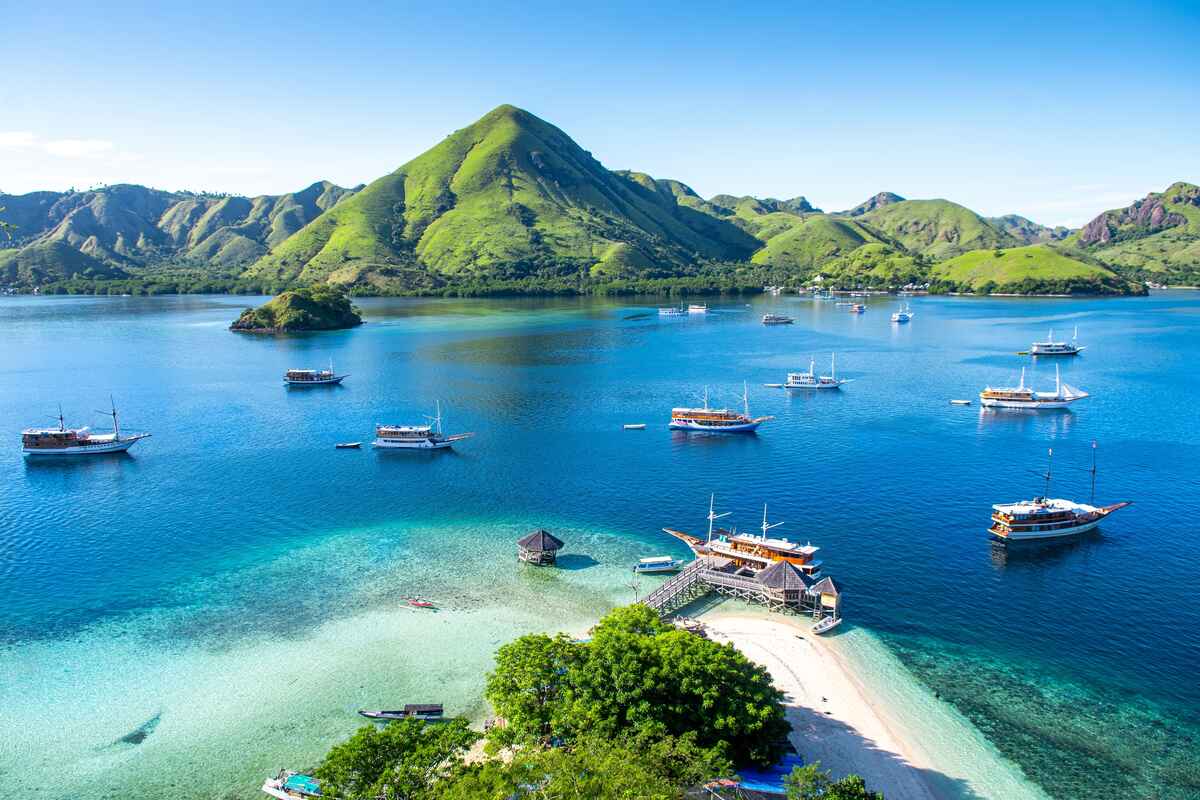 Boats anchored in a tropical bay near an island with wooden structures.