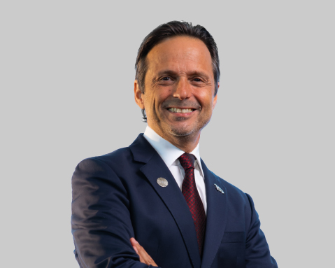 Man in a dark blue suit smiling with arms crossed.