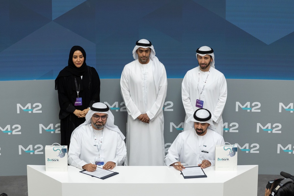 Two men in thobes sign documents at a table with observers and Biobank boxes nearby.