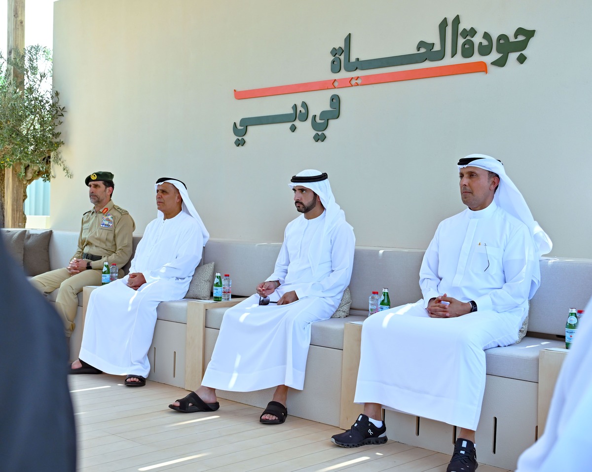 Four men in formal attire sitting outdoors near an Arabic sign.