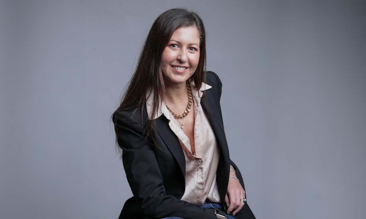 Smiling woman in a blazer against a gray backdrop.