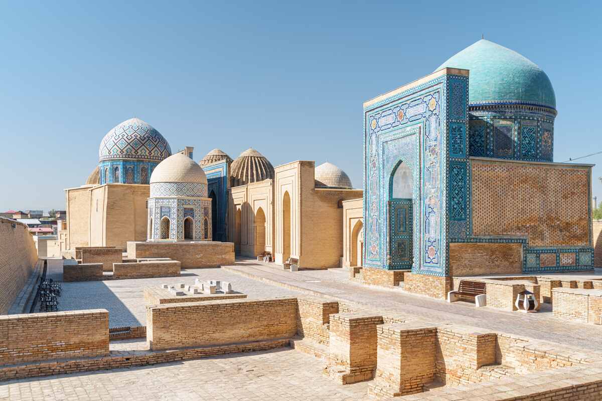 Domed mausoleums with blue tile in sunny courtyard.