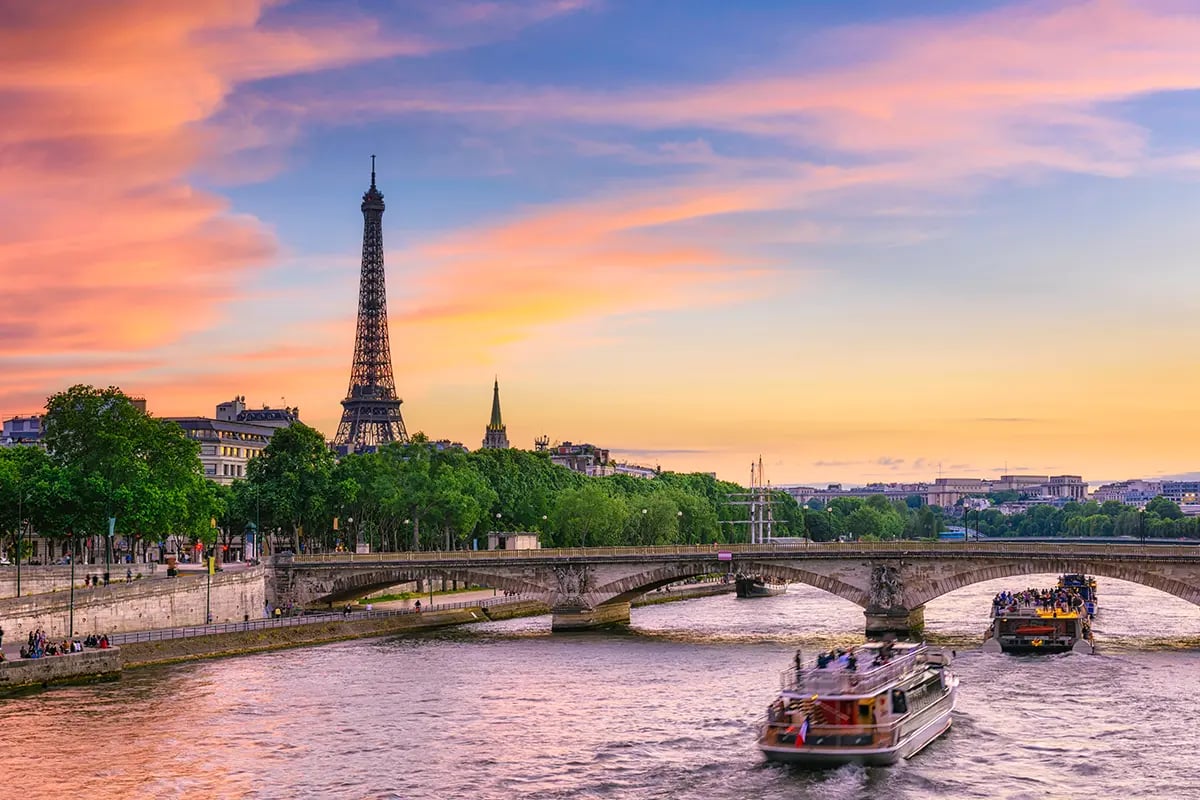 Boats cruise the Seine with the Eiffel Tower at sunset.