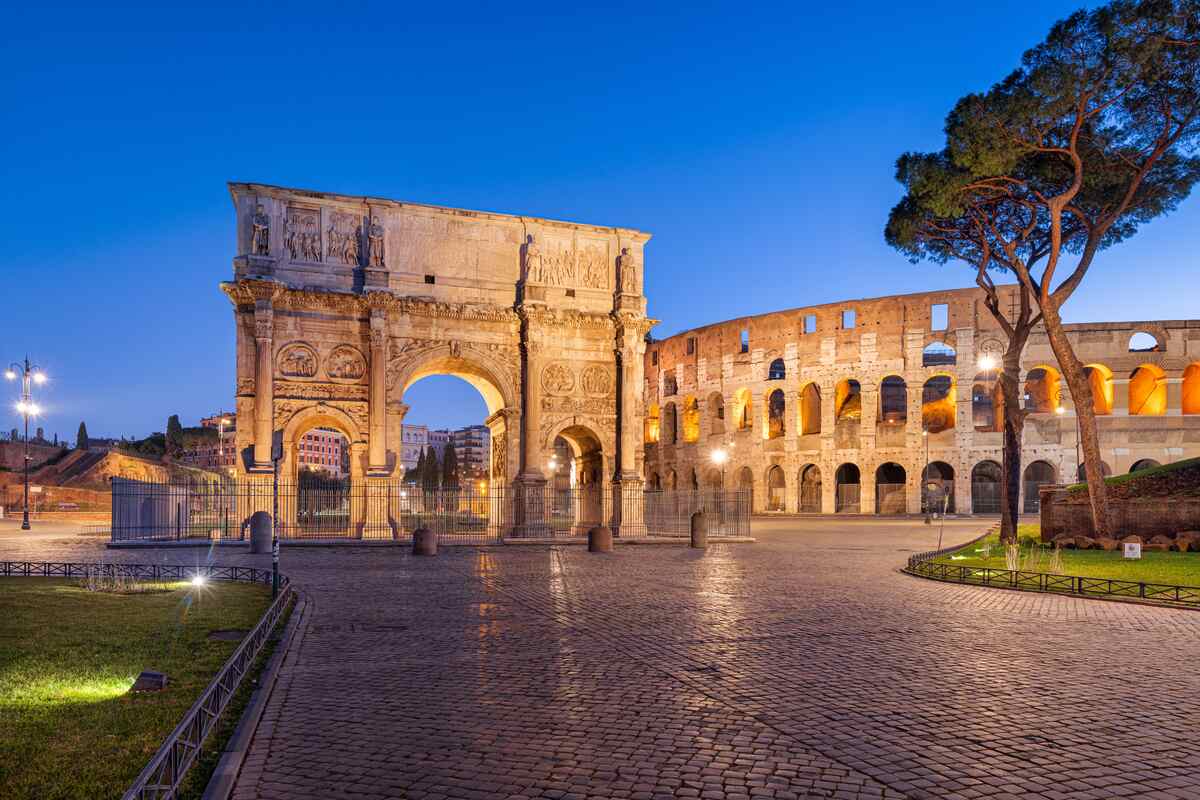 Illuminated Roman arch and Colosseum at twilight.