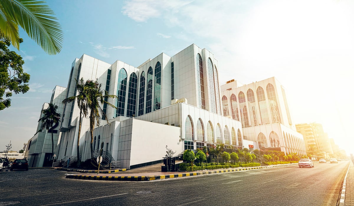 White building with arched windows, palm trees, and parked cars on a sunny day.