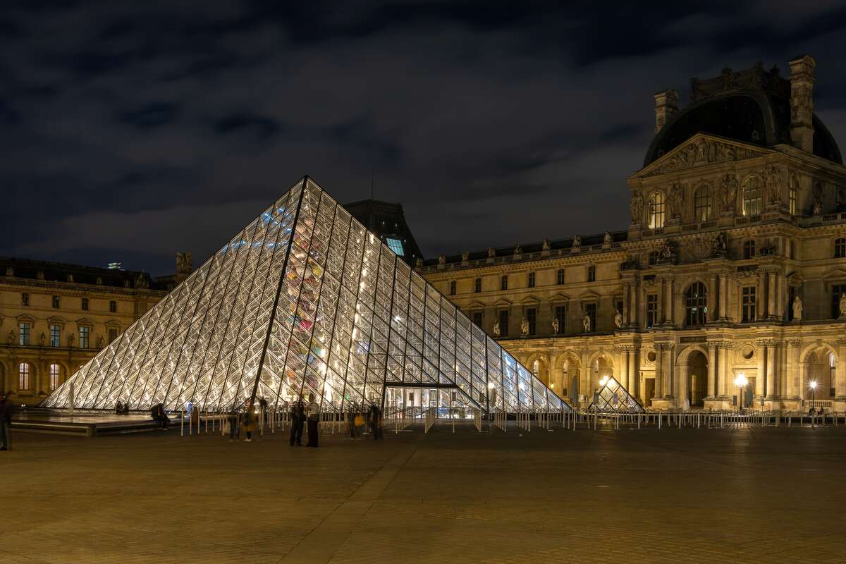 Illuminated glass pyramid at night in front of a classical building.