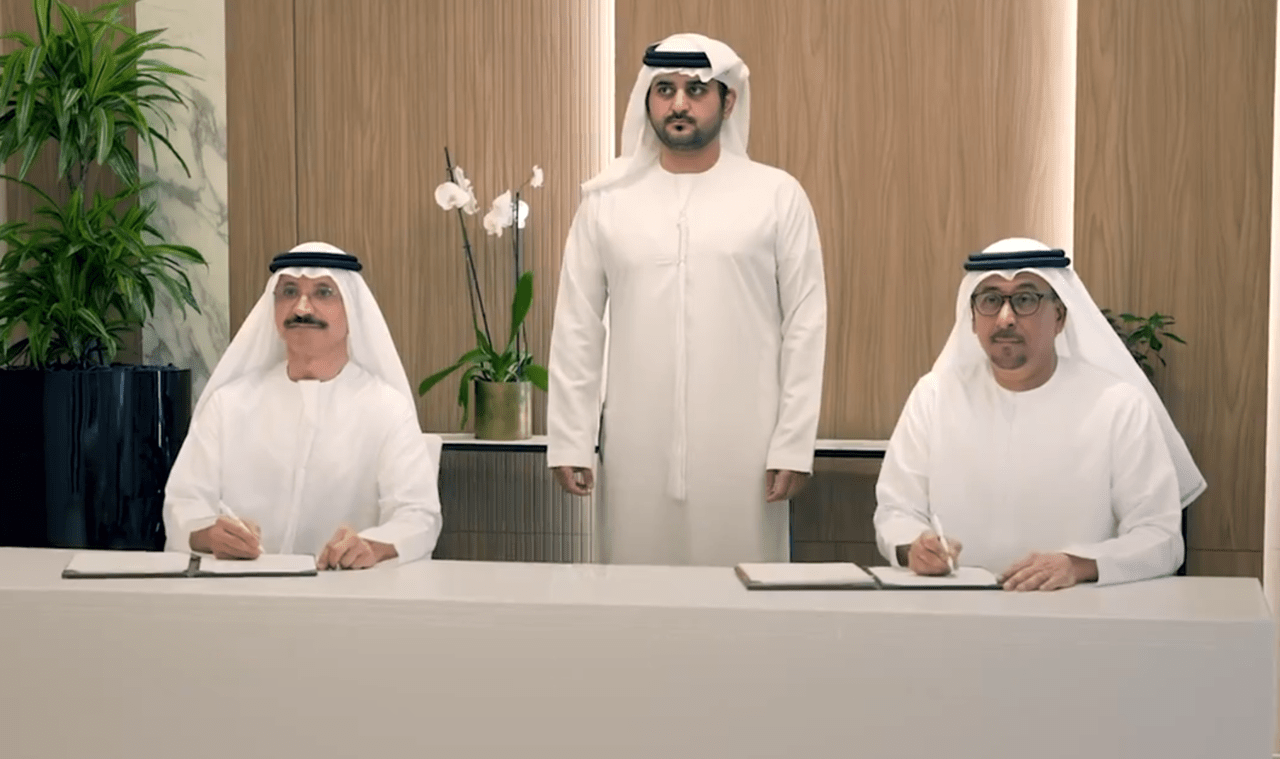 Three men in white thobes signing documents in a modern office.